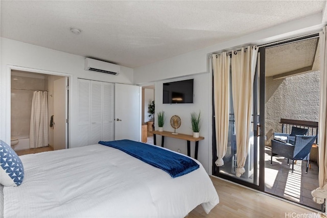 bedroom featuring a textured ceiling, wood finished floors, access to outside, a closet, and a wall mounted AC