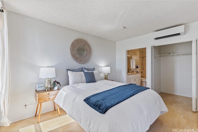 bedroom with light wood-type flooring, an AC wall unit, a textured ceiling, and ensuite bath