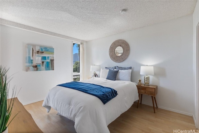 bedroom with a textured ceiling, baseboards, and wood finished floors