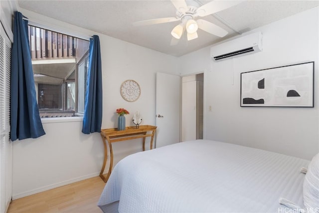 bedroom with baseboards, ceiling fan, wood finished floors, multiple windows, and a wall mounted AC