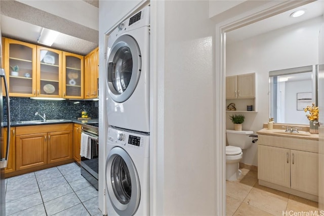 laundry area featuring stacked washer and dryer, light tile patterned floors, laundry area, and a sink