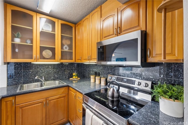 kitchen with tasteful backsplash, glass insert cabinets, stainless steel appliances, and a sink