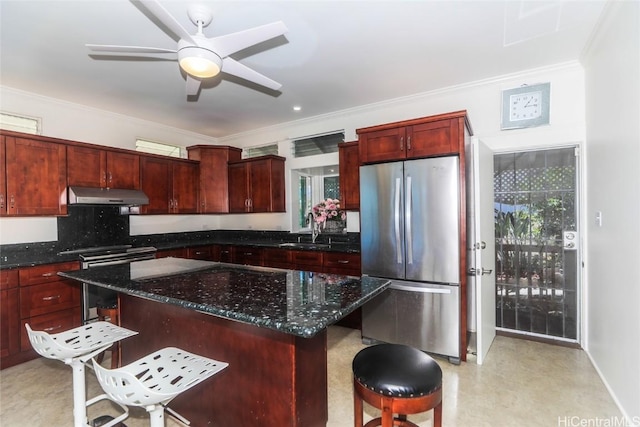 kitchen featuring reddish brown cabinets, a kitchen breakfast bar, freestanding refrigerator, under cabinet range hood, and a sink