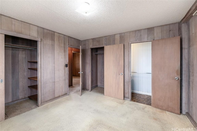 unfurnished bedroom featuring multiple closets, wooden walls, light colored carpet, and a textured ceiling