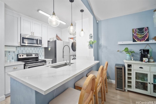 kitchen with a kitchen breakfast bar, stainless steel appliances, sink, stacked washer / dryer, and white cabinets