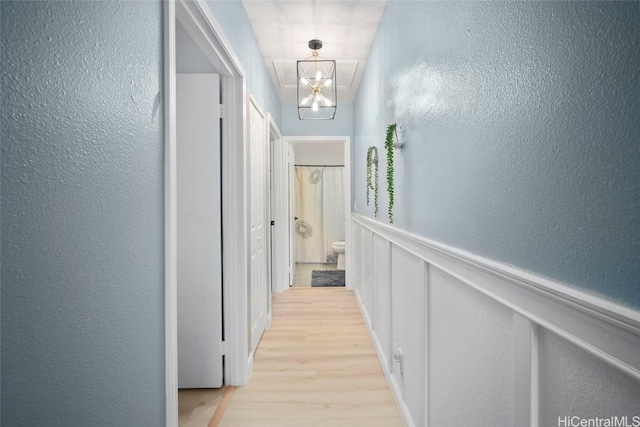 corridor with light wood-type flooring and an inviting chandelier