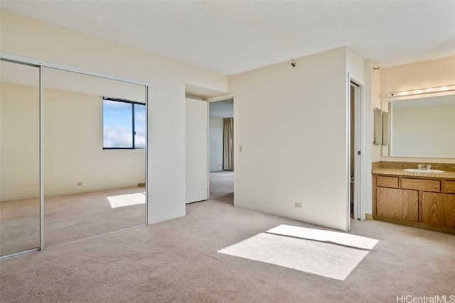 unfurnished bedroom with light colored carpet, ensuite bath, and sink