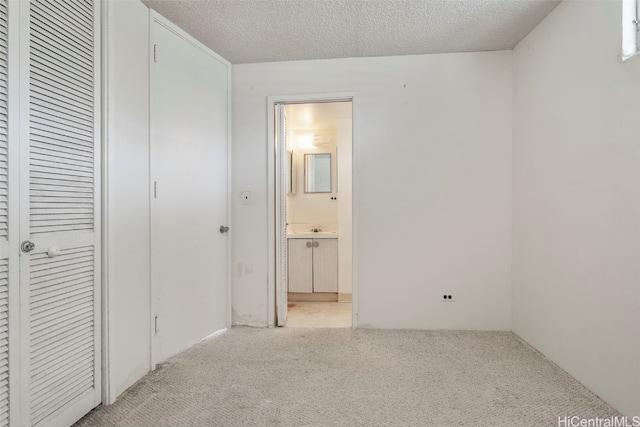 unfurnished bedroom with ensuite bathroom, sink, light colored carpet, and a textured ceiling