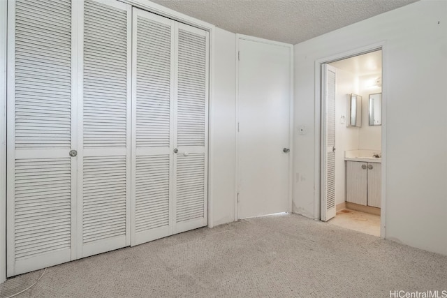 unfurnished bedroom featuring a closet, ensuite bathroom, light carpet, and a textured ceiling