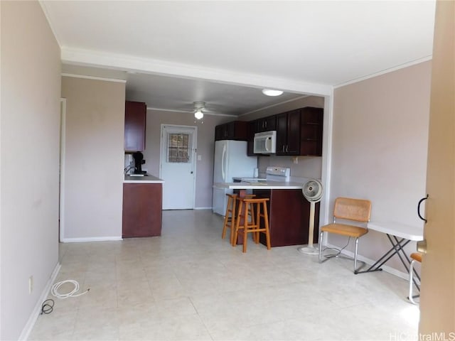 kitchen with a breakfast bar, ceiling fan, white appliances, crown molding, and dark brown cabinetry