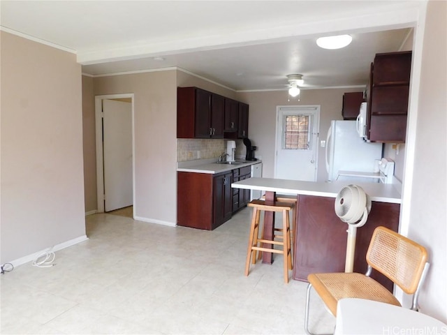 kitchen featuring ceiling fan, decorative backsplash, a kitchen breakfast bar, crown molding, and sink