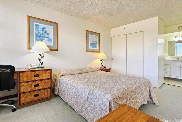 bedroom with a textured ceiling, light colored carpet, ensuite bath, and a closet