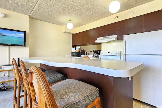 kitchen with stove, white refrigerator, kitchen peninsula, a kitchen bar, and dark brown cabinetry