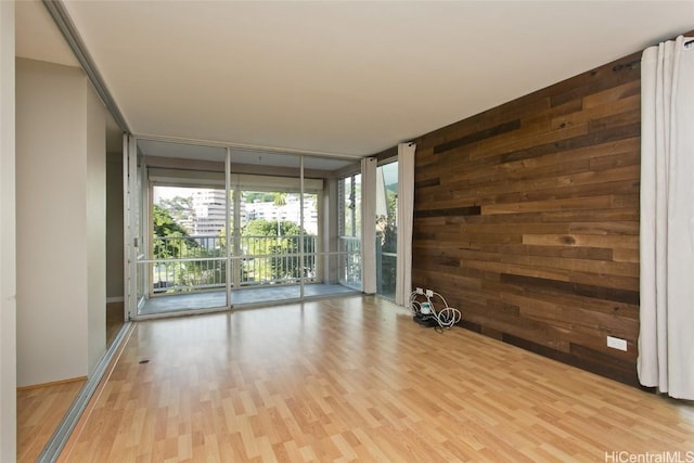 empty room with wood walls, light wood-type flooring, and a wall of windows