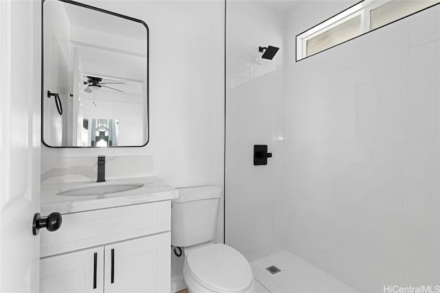 bathroom featuring a tile shower, ceiling fan, vanity, and toilet