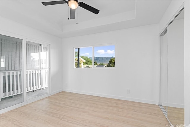 empty room with ceiling fan, light hardwood / wood-style flooring, and a tray ceiling