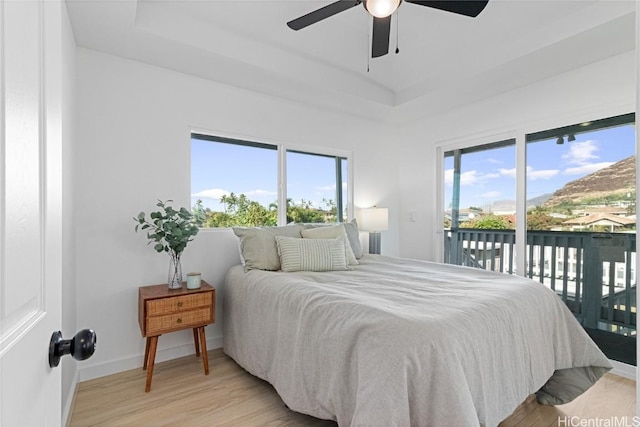 bedroom featuring ceiling fan, light hardwood / wood-style floors, access to exterior, and a tray ceiling