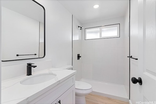 bathroom with tiled shower, vanity, hardwood / wood-style flooring, and toilet