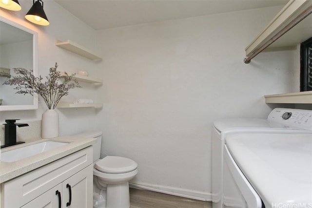 bathroom with hardwood / wood-style floors, vanity, toilet, and washing machine and clothes dryer