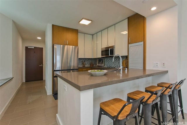 kitchen with kitchen peninsula, sink, backsplash, a breakfast bar, and stainless steel appliances