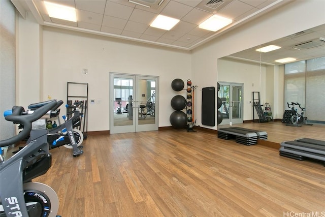 exercise room featuring light hardwood / wood-style floors, a high ceiling, a paneled ceiling, and french doors