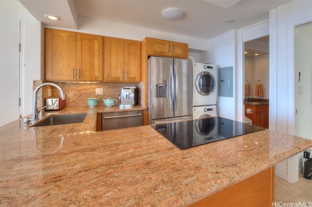 kitchen featuring sink, backsplash, kitchen peninsula, stacked washer and clothes dryer, and appliances with stainless steel finishes