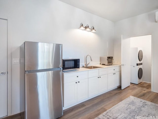 kitchen with stainless steel fridge, light wood-type flooring, stacked washing maching and dryer, sink, and white cabinets