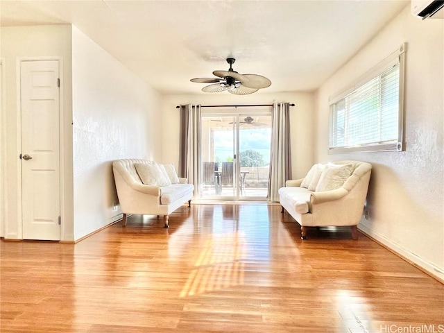 sitting room with an AC wall unit, ceiling fan, and light wood-type flooring