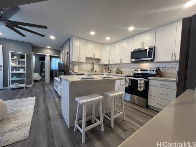 kitchen with ceiling fan, a center island, stainless steel appliances, dark hardwood / wood-style flooring, and white cabinets