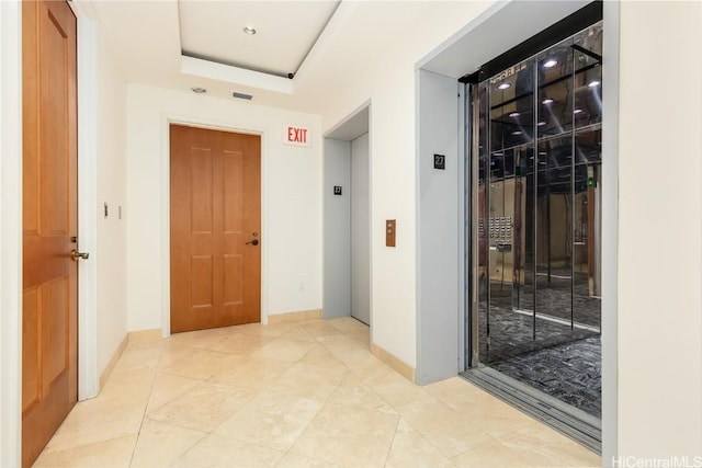 hallway with a raised ceiling, elevator, and light tile patterned floors