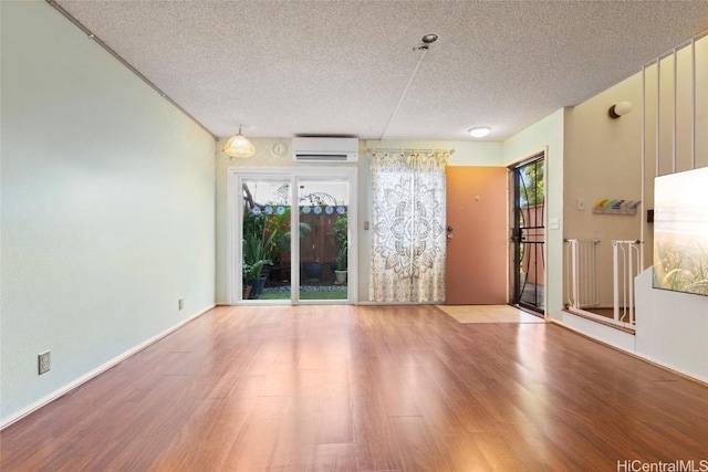 empty room with a wall unit AC, a textured ceiling, and wood-type flooring