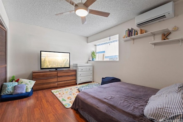 bedroom with ceiling fan, a wall mounted AC, a textured ceiling, and wood-type flooring