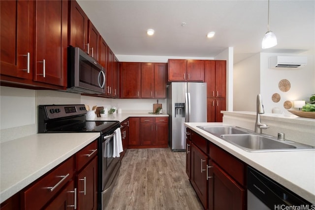 kitchen featuring a wall mounted air conditioner, hanging light fixtures, sink, appliances with stainless steel finishes, and light hardwood / wood-style floors