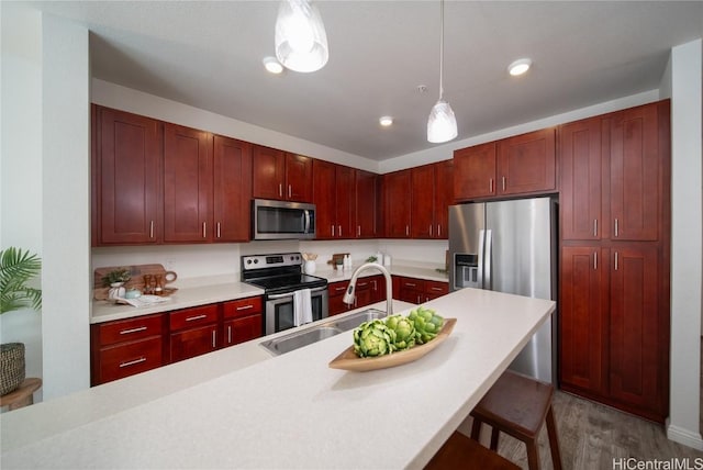 kitchen with sink, stainless steel appliances, pendant lighting, light hardwood / wood-style floors, and a kitchen bar