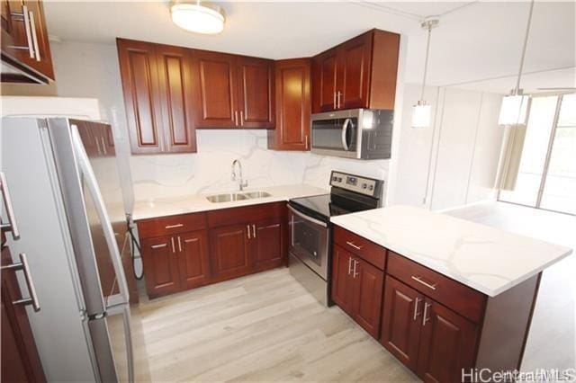 kitchen featuring light wood-type flooring, light stone counters, stainless steel appliances, sink, and hanging light fixtures