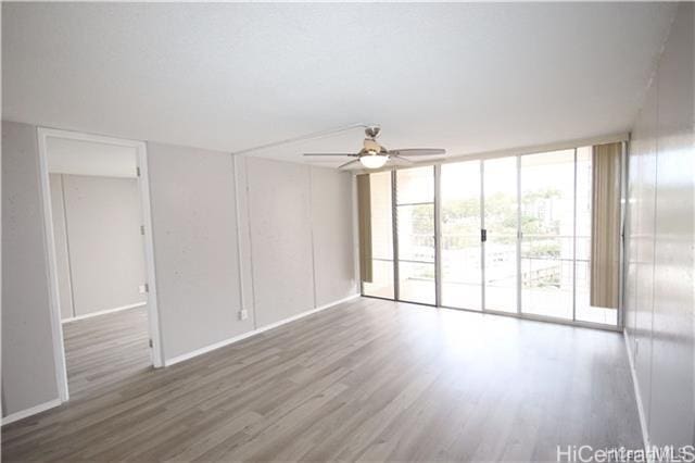 unfurnished room featuring hardwood / wood-style flooring, plenty of natural light, a wall of windows, and ceiling fan