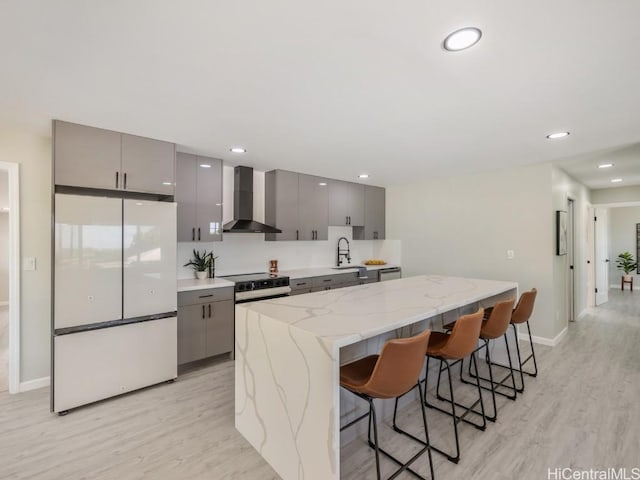 kitchen featuring wall chimney exhaust hood, gray cabinets, a kitchen breakfast bar, and white appliances