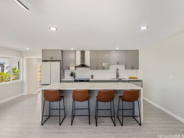 kitchen featuring gray cabinetry, wall chimney exhaust hood, sink, and a breakfast bar area