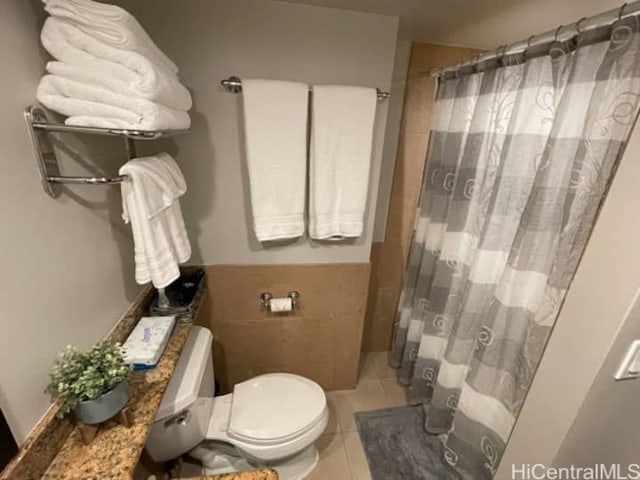 bathroom with toilet, a shower with shower curtain, tile patterned floors, and tile walls