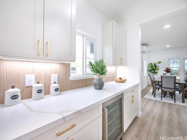 kitchen featuring a wall mounted air conditioner, wine cooler, light hardwood / wood-style flooring, light stone counters, and white cabinetry