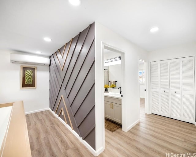 hallway with a wall mounted AC, sink, and light wood-type flooring