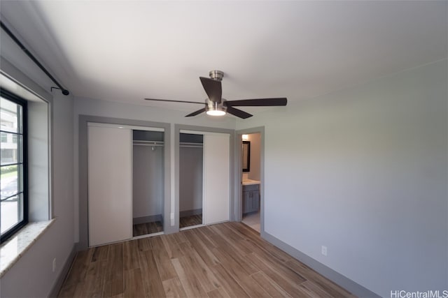 unfurnished bedroom featuring connected bathroom, light hardwood / wood-style floors, ceiling fan, and multiple closets