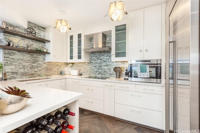 kitchen featuring pendant lighting, wall chimney exhaust hood, backsplash, white cabinets, and stainless steel oven