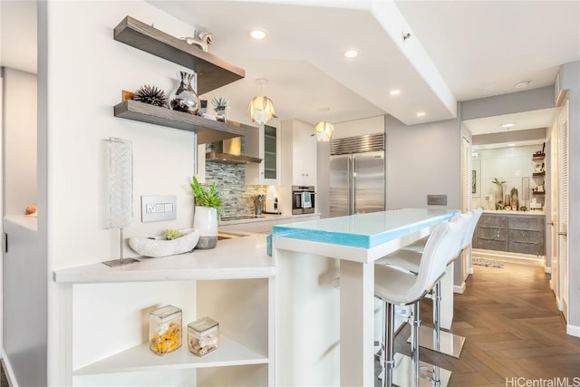 kitchen with appliances with stainless steel finishes, decorative backsplash, parquet flooring, kitchen peninsula, and a breakfast bar area