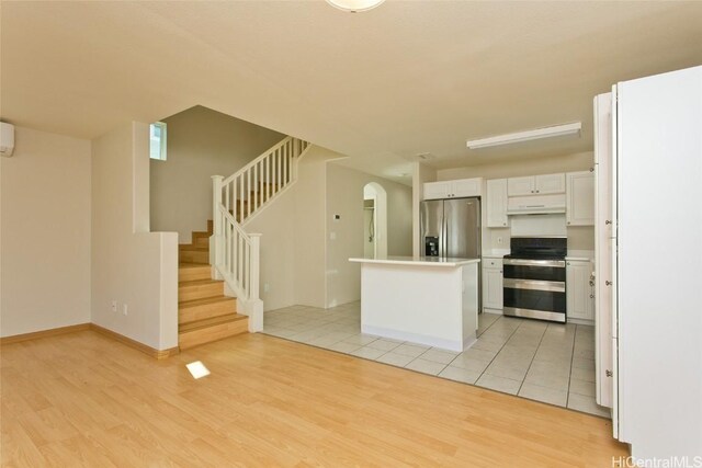 kitchen featuring light wood-type flooring, a wall mounted AC, a kitchen island, white cabinetry, and stainless steel appliances