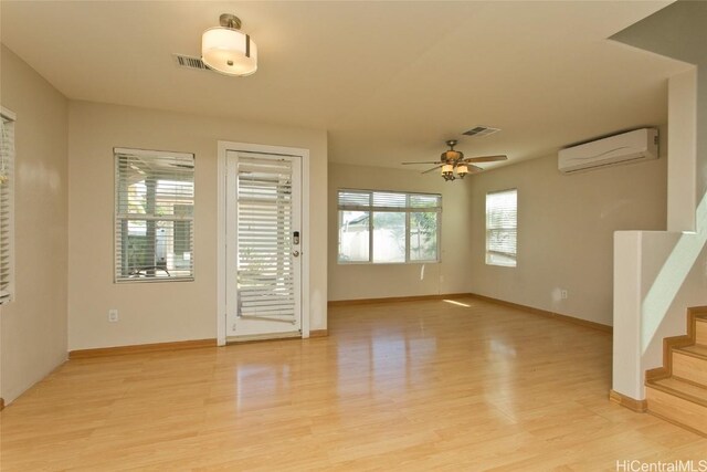 unfurnished living room with a wall unit AC, ceiling fan, and light hardwood / wood-style floors