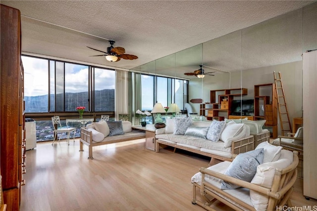 living room with ceiling fan, expansive windows, a textured ceiling, and light hardwood / wood-style flooring