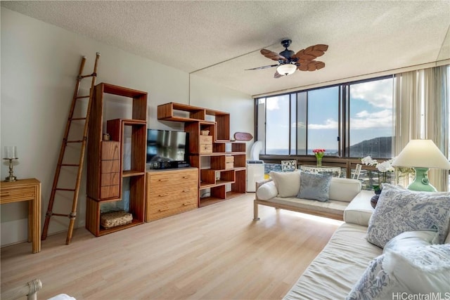 living room featuring ceiling fan, expansive windows, light hardwood / wood-style floors, and a textured ceiling