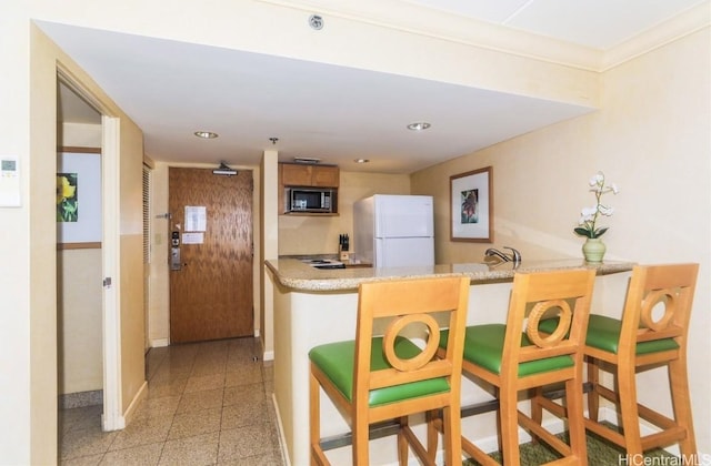 kitchen with a kitchen bar, kitchen peninsula, white fridge, and ornamental molding