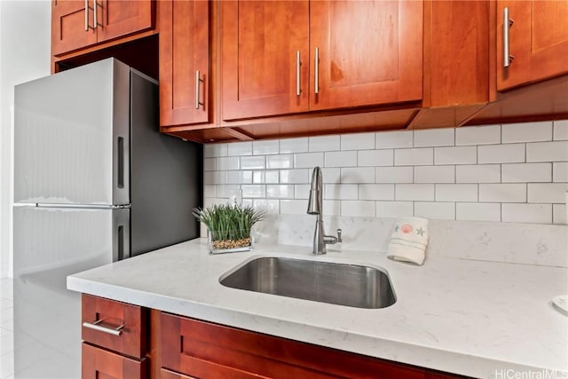 kitchen with sink, light stone counters, decorative backsplash, and stainless steel refrigerator